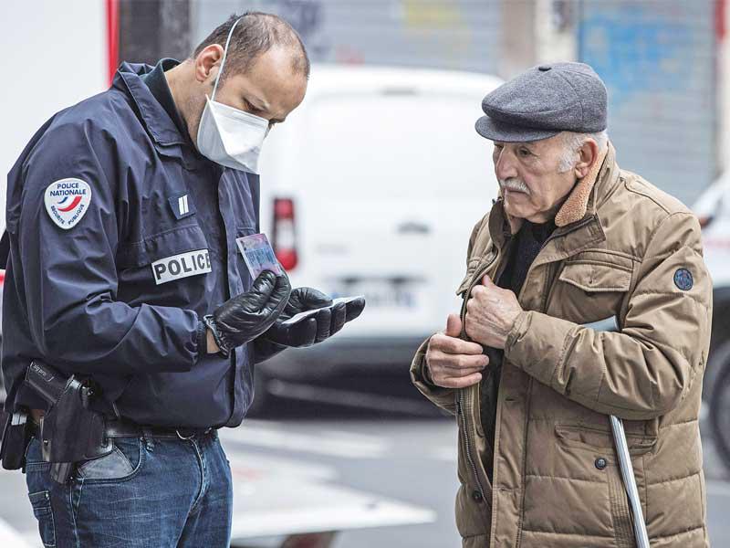شرطي فرنسي يدقق بـ «إذن الخروج» الخاص برجل مسن في باريس أمس (أ ف ب) 