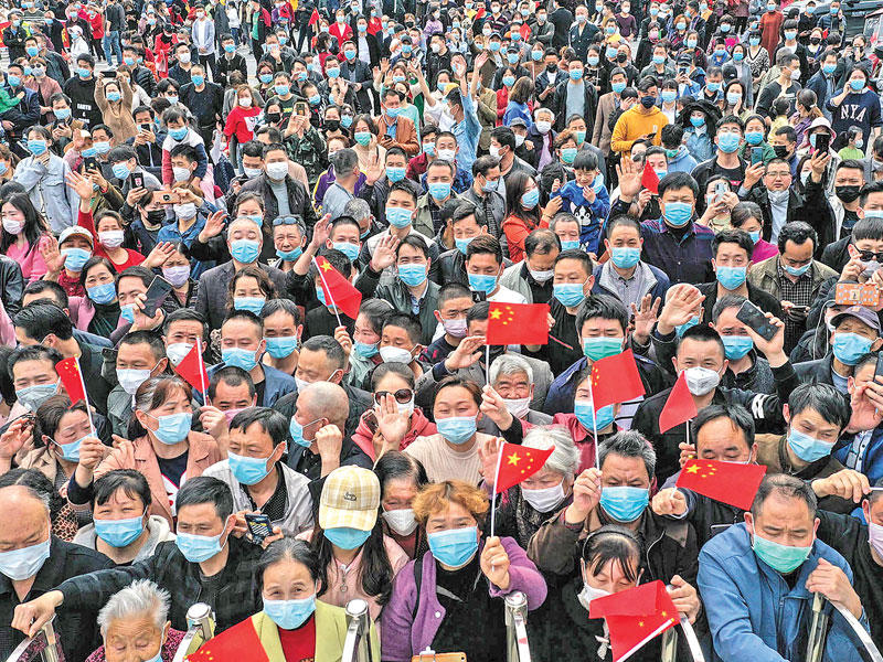 صينيون يضعون أقنعة واقية يلوّحون بعلم بلادهم كتعبير عن شكرهم للأطباء الذين ساعدوهم على الشفاء من الفيروس في مقاطعة يونمينغ (أ ف ب)