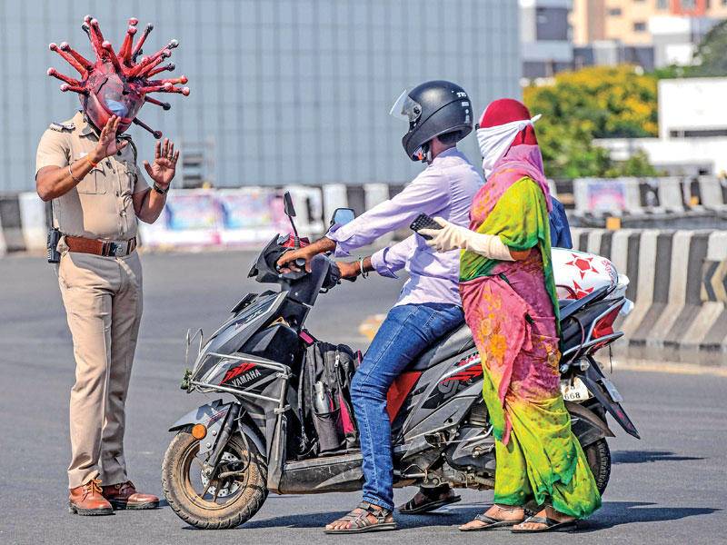شرطي هندي يضع قناعاً على شكل «فيروس» يوقف زوجين خرقا حظر التجوّل في مدينة شيناي أمس (أ ف ب)