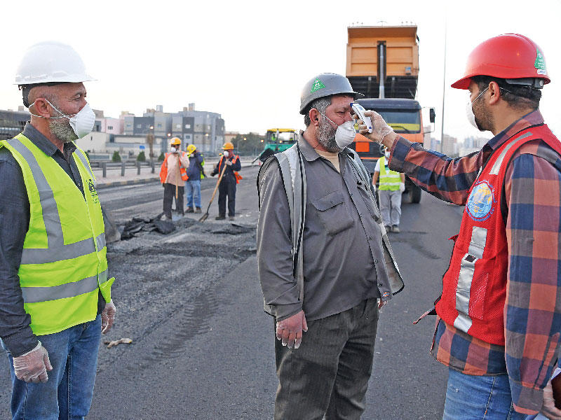 تظهر الصورة جانباً من عملية الإصلاح على طريق الفحيحيل السريع مع قياس درجة الحرارة لأحد الفنيين الموجودين في الموقع. (تصوير عبدالله الخلف)