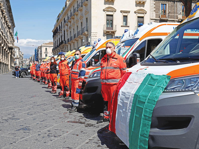 عاملون في المجال الطبي يقفون دقيقة صمت أمام سيارات الاسعاف حداداً على ضحايا «كورونا» في مدينة كاتانيا الإيطالية أمس (رويترز) 