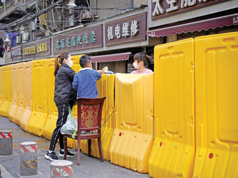 صينية مع ابنها يتسوقان من خلف الجدار في ووهان أمس  (رويترز)