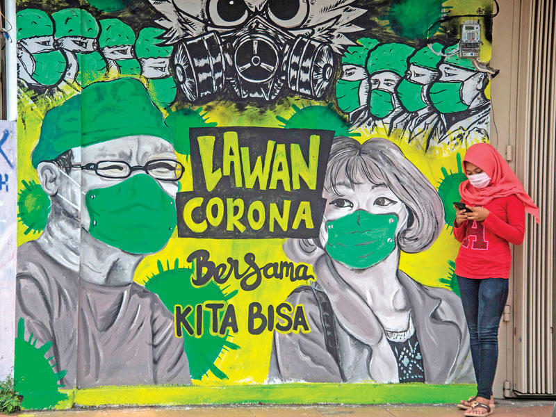 إندونيسية تستخدم هاتفها أمام جدارية عن «كورونا» في مدينة بانغكالان أمس    (أ ف ب)
