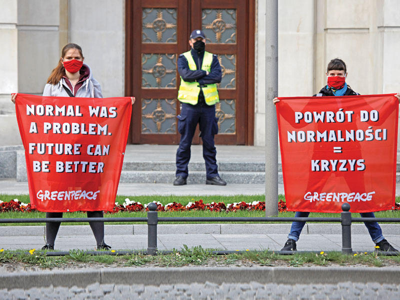 ناشطان من  غرينبيس خلال احتجاج امام مقر رئيس وزراء بولندا يحمل أحدهما لافتة كتب عليها «الطبيعي كان مشكلة . يمكن أن يكون المستقبل أفضل» في اشارة الى رفع قيود كورونا (رويترز)  