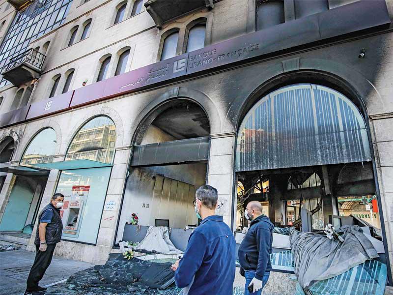 لبنانيون يتفقّدون الأضرار التي لحقت بأحد المصارف في طرابلس أمس (أ ف ب)