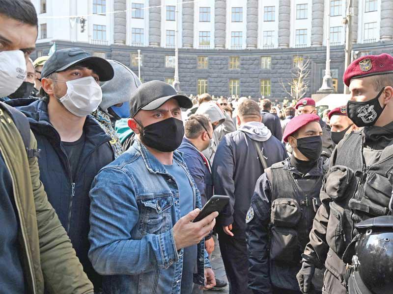 رجال أمن ومتظاهرون يحتجون على قيود فيروس كورونا يرتدون الكمامات في كييف أمس (أ ف ب) 