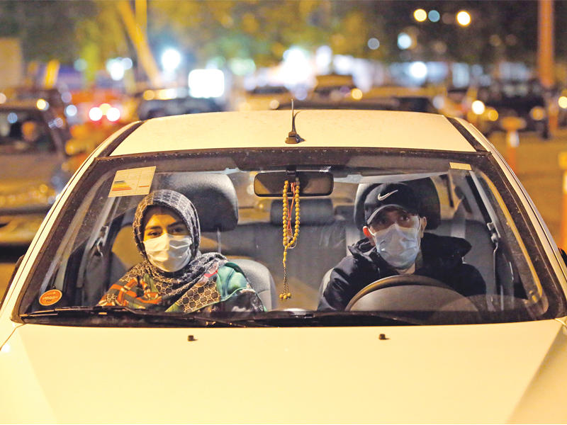 إيرانيون في سياراتهم يتابعون شعائر دينية تبث على شاشة عملاقة أمامهم خلال شهر رمضان في طهران (أي بي أيه)