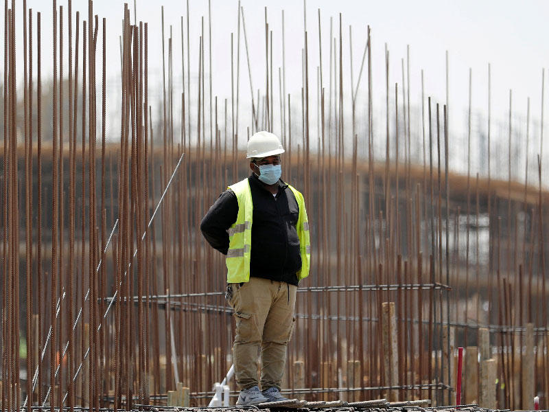 عامل يرتدي قناع وجه واقٍ يقف على مبنى قيد الإنشاء في العاصمة الإدارية الجديدة