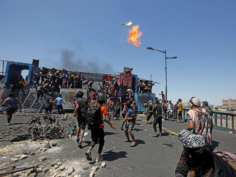 عراقي يلقي زجاجة حارقة خلال تجمع على جسر الجمهورية ببغداد أمس (رويترز)