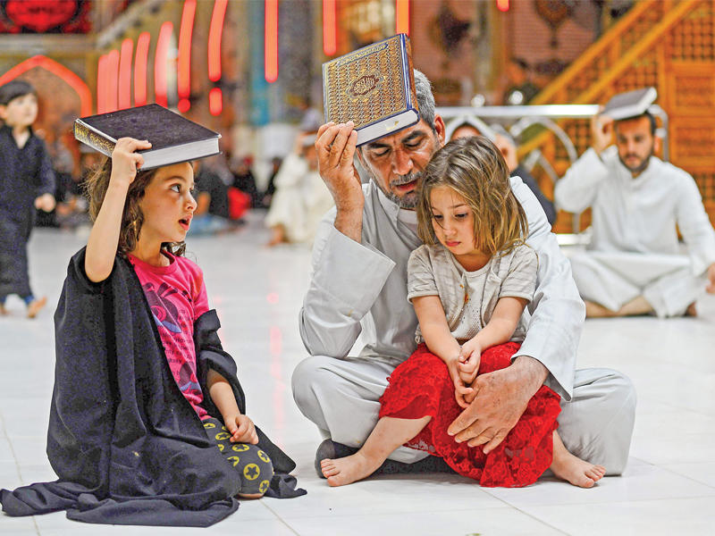 عراقي وابنتاه يضعون المصحف الشريف على رؤوسهم خلال إحياء طقوس ليلة القدر في النجف مساء أمس الأول    (أ ف ب)