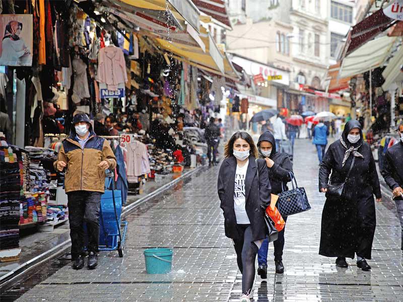 متسوقون يضعون كمامات تحت المطر في أحد أسواق إسطنبول أمس (رويترز)n