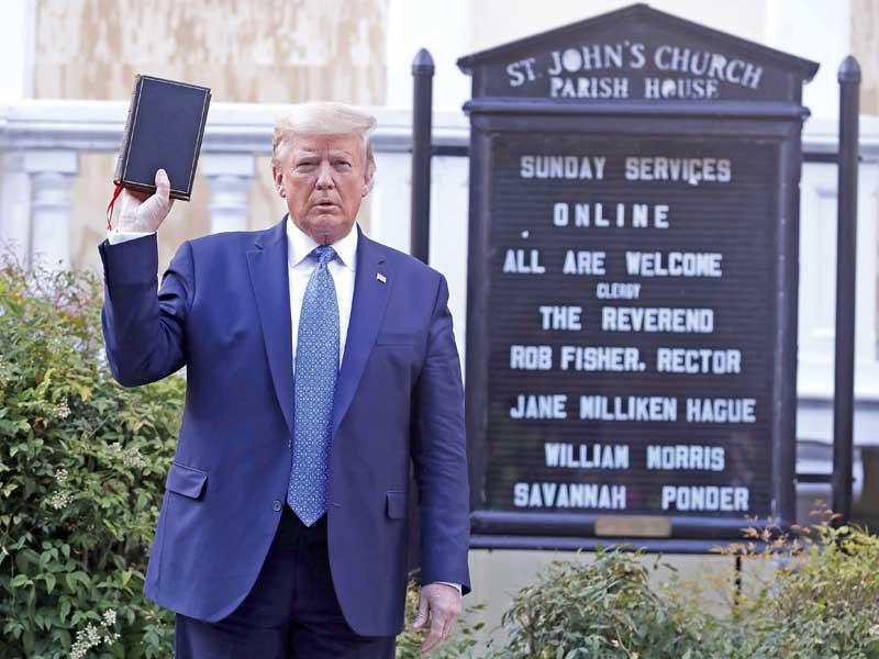ترامب يرفع نسخة من الإنجيل أمام كنيسة سانت جون قرب البيت الأبيض أمس الأول  (إي بي أيه)