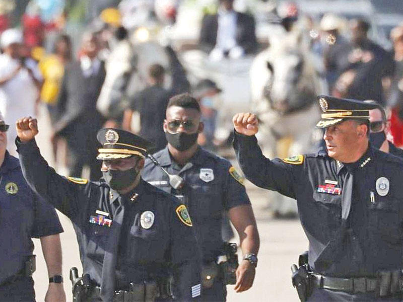 رئيس شرطة هيوستن آرت أسيفيدو (يمين) وضابط آخر يرفعون أيديهم أثناء المشي أمام النعش الذي يحتوي على بقايا جورج فلويد