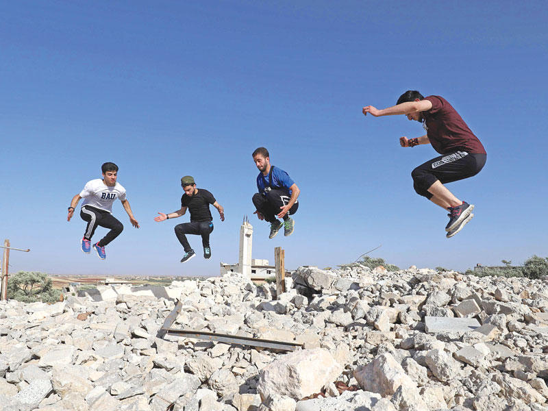 سوريون يمارسون رياضة الباركور بين ركام المباني في إدلب  (أ ف ب)