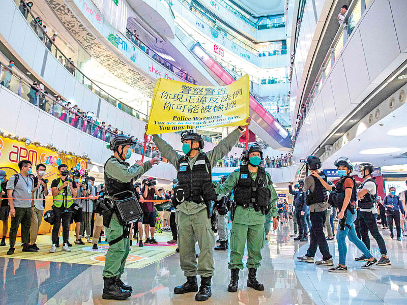 شرطي يرفع لافتة تحذّر متظاهرين من مغبة اعتقالهم في أحد المجمعات التجارية بهونغ كونغ (ا ف ب)