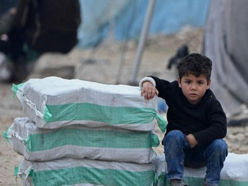 صبي سوري نازح يجلس بجانب المساعدات الإنسانية  ويتألف من مواد التدفئة ومياه الشرب  في مخيم في بلدة المحمدية 