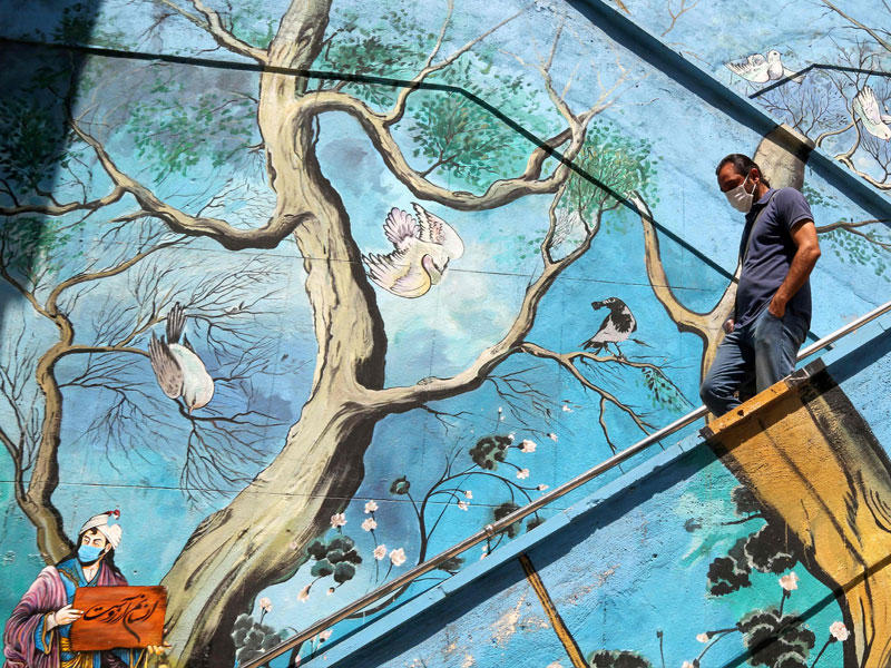 إيراني يرتدي كمامة يجتاز سلالم مزينة في طهران  (أ ف ب)