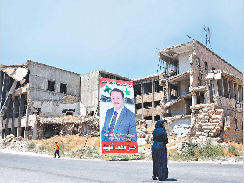 سورية تمر أمام لافتة مرشح على منزل مدمر في حلب أمس الأول t(أ ف ب)