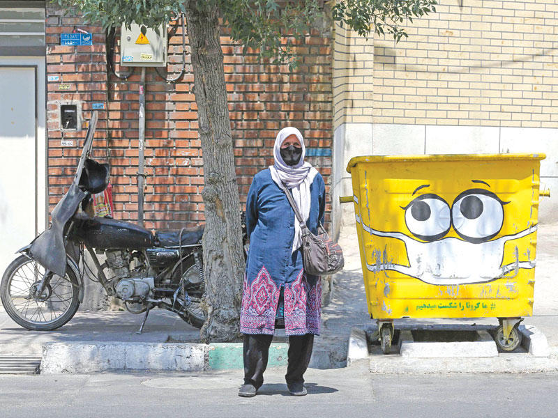 سيدة إيرانية تقف بالقرب من حاوية نفايات مرسوم عليها كمامة في طهران أمسt (أ ف ب)