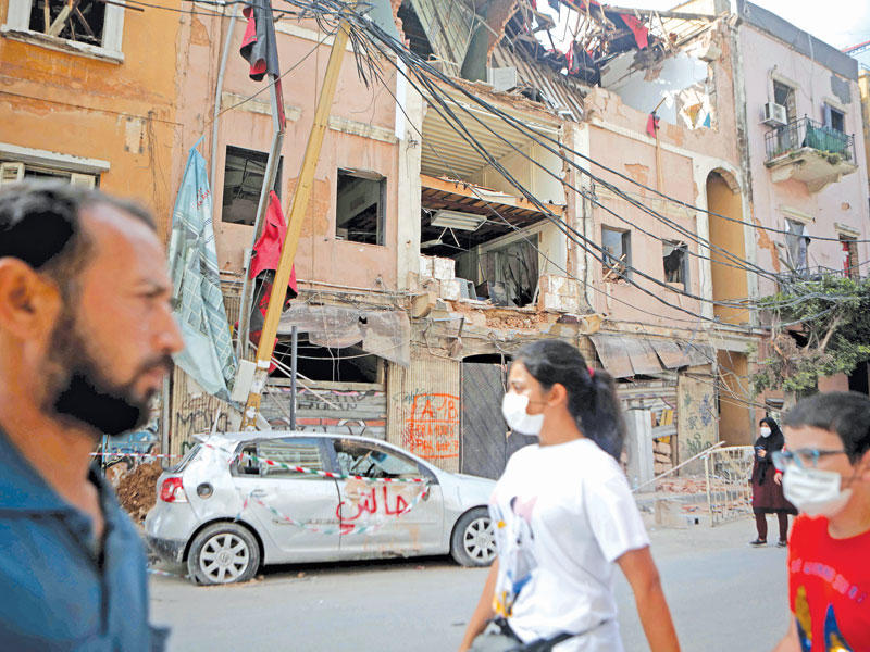 لبنانيون يمرون أمام مبنى تضرر بانفجار المرفأ في حي مار مخايل الذي تسكنه غالبية مسيحية ببيروت أمس t(أ ف ب)