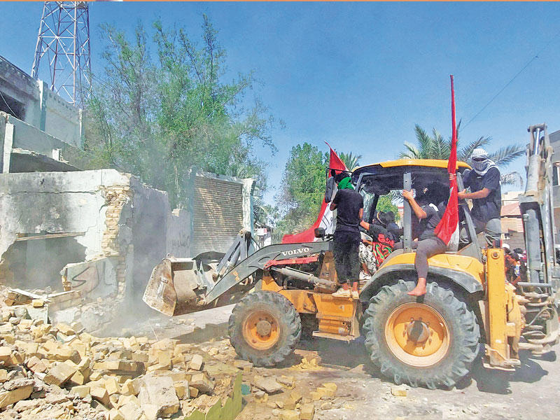 محتجون يستخدمون جرافة لهدم أحد مقار الأحزاب في الناصرية أمس (رويترز)