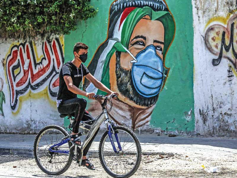 فلسطيني يمر أمام جدارية توعية بخطر «كورونا» في غزة أمس الأول (أ ف ب)