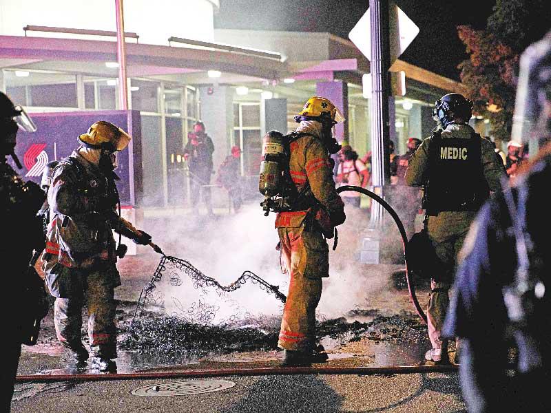 رجال الإطفاء يخمدون حريقاً أشعله متظاهرون بمبنى شرطة بورتلاند أمس الأول (أ ف ب)