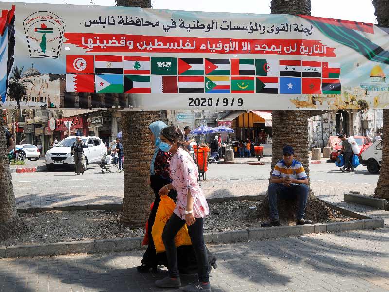 سيدتان تمرّان قرب لافتة عليها أعلام بعض الدول العربية في نابلس أمس (رويترز)