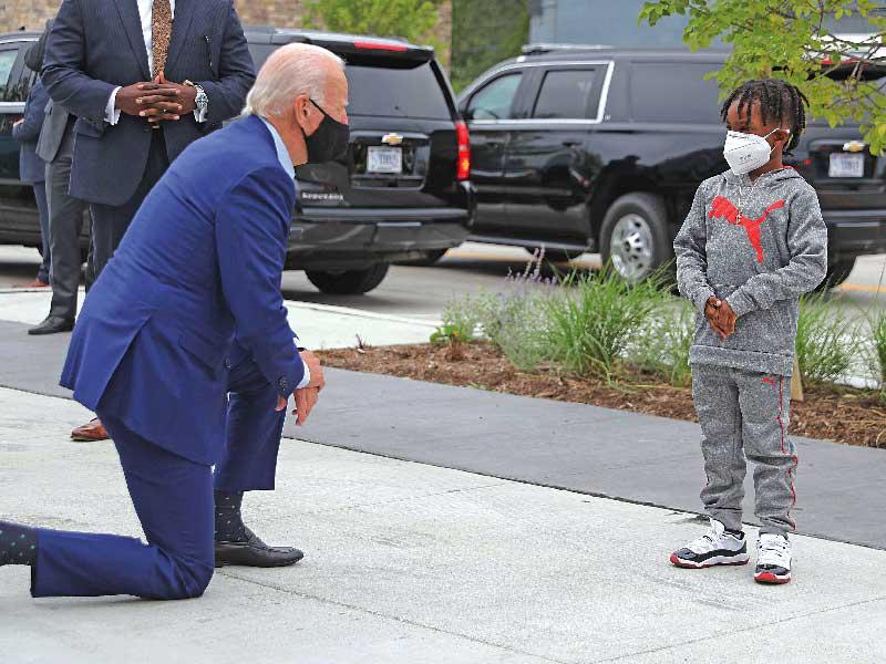 جو بايدن يركع للتحدث مع صبي خلال زيارته أحد أسواق ديترويت أمس الأول (أ ف ب)n