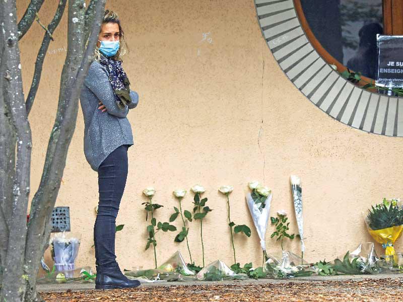 فرنسية تقف حيث وضعت مئات الورود والبطاقات أمام المدرسة حيث كان يعمل أستاذ التاريخ في كونفلان أمس          (رويترز) 