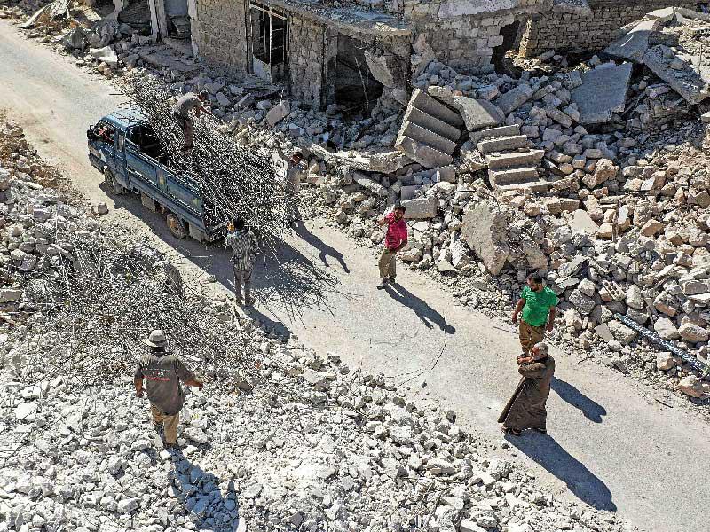 سوريون يجمعون القضبان الحديدية من بين أنقاض المباني المدمرة بمناطق سيطرة المعارضة في إدلب أمس الأول (أ ف ب)