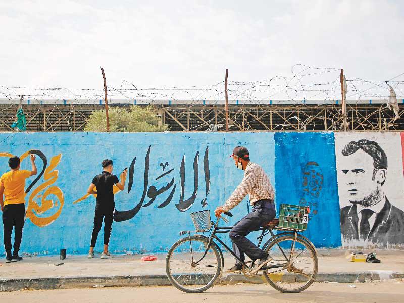 فلسطينيان يرسمان «غرافيتي» ضد ماكرون في مخيم النصيرات في غزة أمس (أ ف ب)