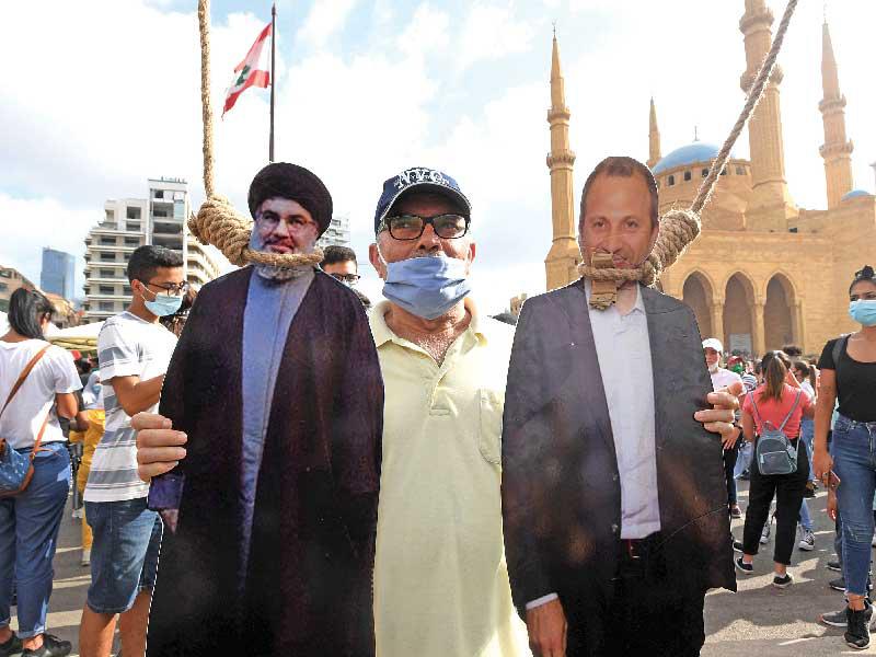 لبناني يرفع صورتين لجبران باسيل وحسن نصرالله خلال تظاهرة مناهضة للحكومة في بيروت في أغسطس الماضي (ا ف ب)