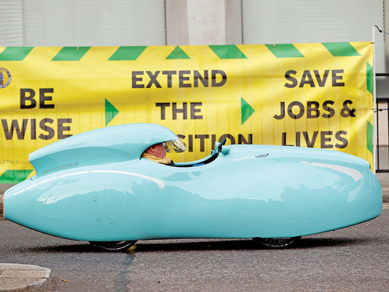 بريطاني يقود دراجة على شكل سيارة يمر أمام لافتة احتجاجية بالتزامن مع مفوضات أوروبية - بريطانية بشأن بريكست أمسt(رويترز)