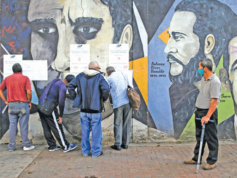 فنزويليون يدقّقون بلوائح الأسماء خارج أحد مقار الاقتراع في كاراكاس أمس (رويترز)