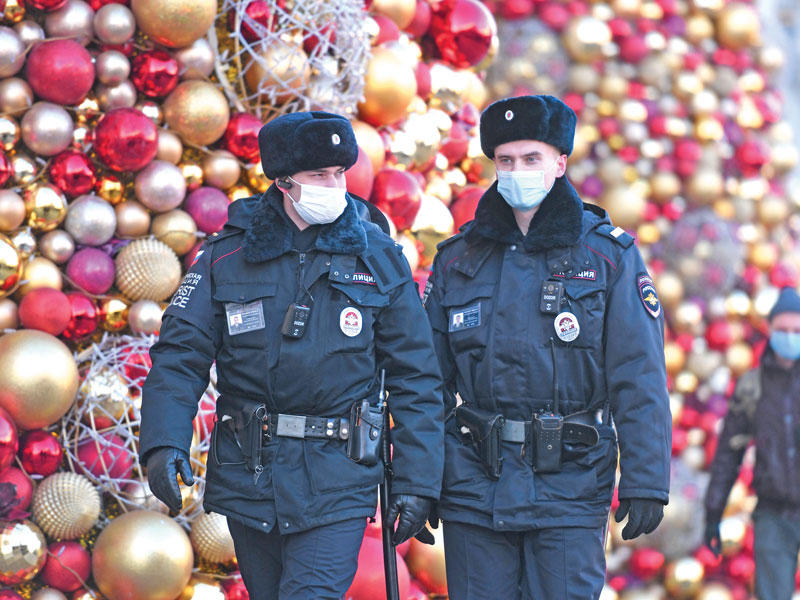 شرطيان روسيان يضعان كمامتين يمرّان قرب زينة الميلاد في موسكو أمس   (ا ف ب)
