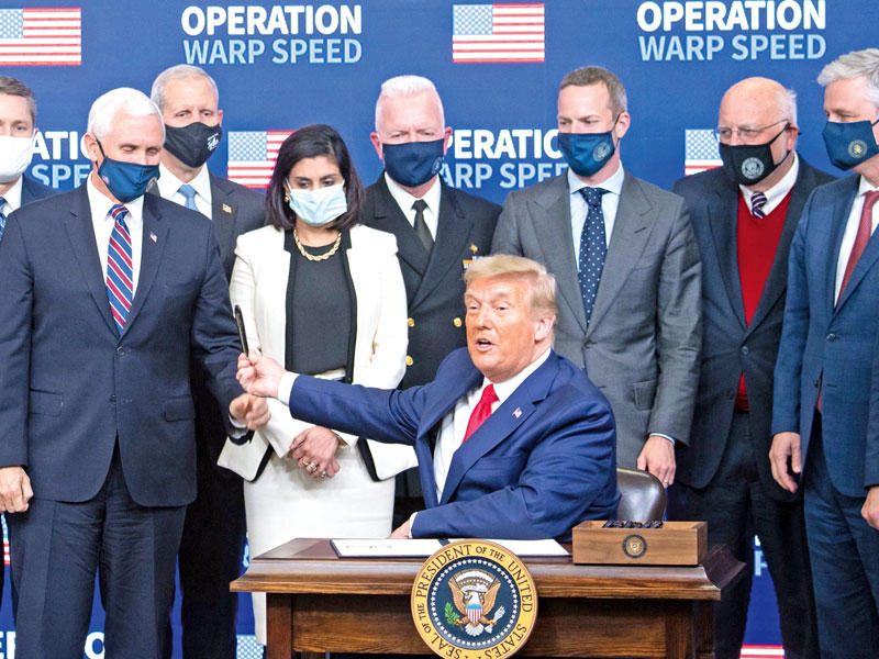 دونالد ترامب يسلم قلماً لنائبه مايك بنس بعد التوقيع على إعطاء الأولوية للأميركيين لتلقي لقاحات كورونا في البيت الأبيض أمس الأول (أ ف ب)