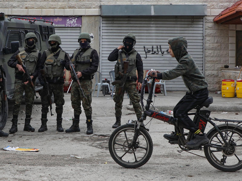 فتى فلسطيني يمر أمام عناصر أمنية فلسطينية في مخيم بلاطة  (أ ف ب)