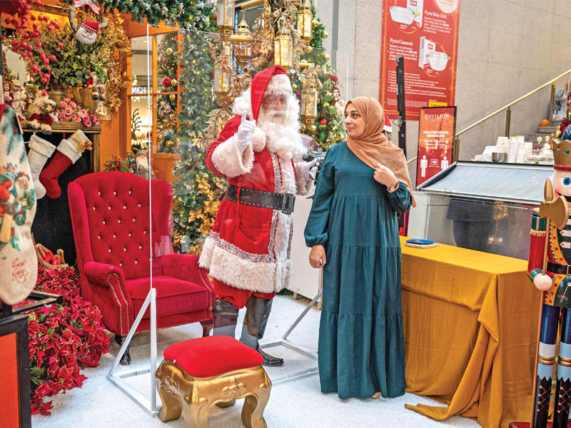 سيدة ماليزية تتحدّث مع «سانتاكلوز» داخل غرفة عازلة في أحد متاجر كوالالمبور أمس (أ ف ب)