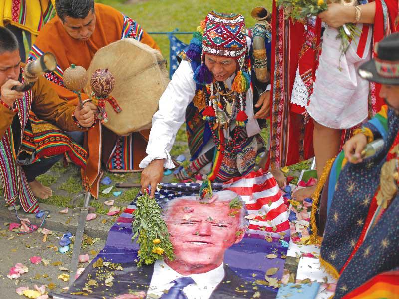 كاهن من البيرو ينظف صورة بايدن خلال طقوس في ميدان سان مارتن في ليما أمس الأول (إي بي إيه)