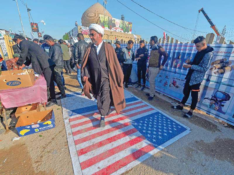 عراقيون يدوسون على علم أميركي خلال توجههم إلى مدافن وادي السلام في النجف لزيارة قبر أبومهدي المهندس (أ ف ب)  