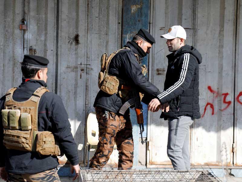 أحد أفراد قوة الأمن العراقية يتفقد رجلاً بالقرب من موقع الضرر في أعقاب هجوم انتحاري في سوق مركزي في بغداد