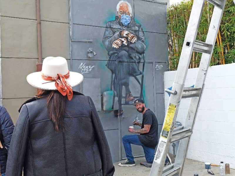 فنان يرسم جدارية في كاليفورنيا لصورة بيرني ساندرز الشهيرة خلال تنصيب بايدن (أ ف ب)