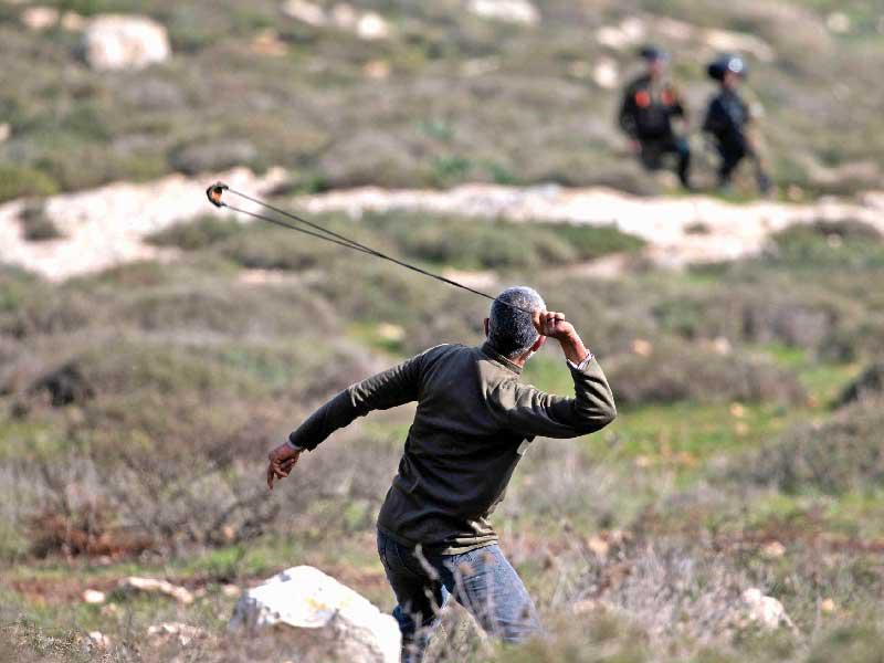 فلسطيني يواجه بالمقلاع جنوداً إسرائيليين قرب نابلس بالضفة الغربية المحتلة أمس      (أ ف ب) 
