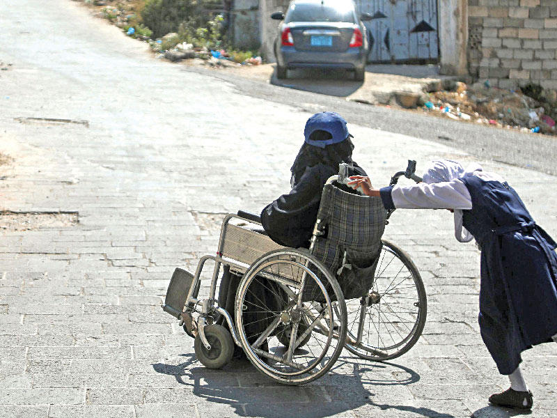 طفلة يمنية في تعز تساعد والدتها المقعدة بعد إصابتها في قصف (أ ف ب)