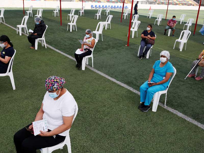 عاملو صحة بانتظار دورهم بملعب لكرة القدم لتلقيهم التطعيم ضد «كورونا» في البيرو أمس الأول (رويترز)