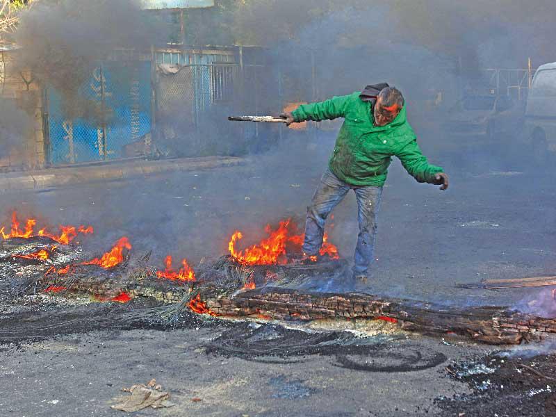 متظاهر يغذي ناراً أشعلها محتجون لقطع الطريق الساحلي بين بيروت وصيدا أمس (أ ف ب)