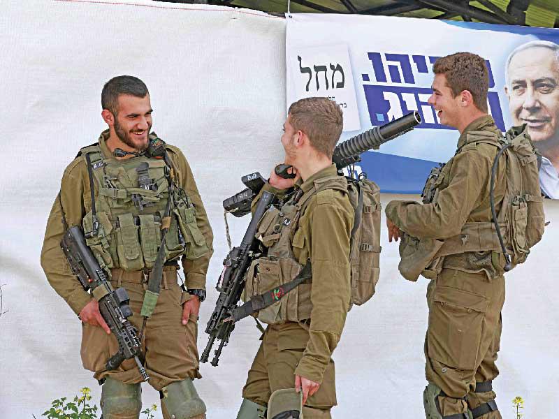 جنود قرب ملصق دعائي لنتنياهو بالضفة الغربية المحتلة أمس     (أ ف ب)