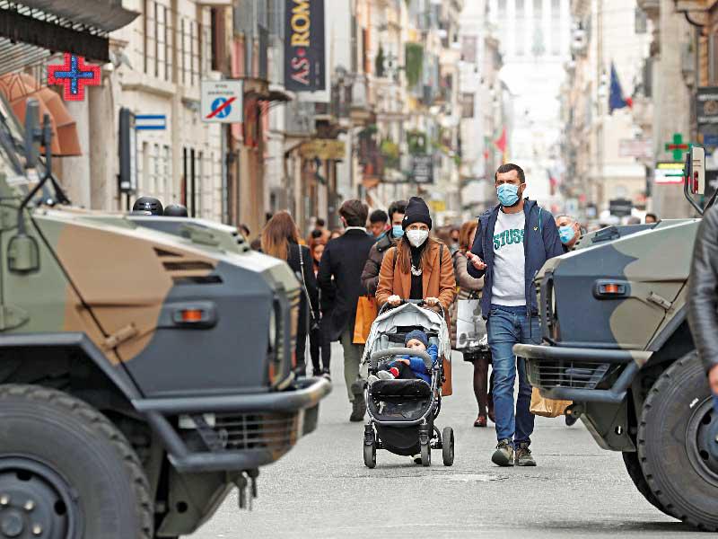 إيطاليون يمرّون قرب آليات عسكرية قبل ساعات من الإقفال العام الجديد في روما أمس (رويترز)