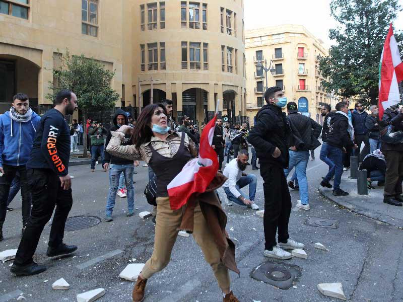 متظاهرة تقذف الحجارة على بوابة محصنة تؤدي إلى مبنى البرلمان اللبناني